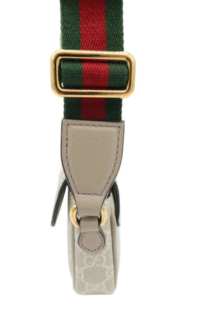 A close-up of a shoulder strap featuring a green and red web stripe with a gold-tone metal buckle, attached to a beige leather tab and a light beige monogram canvas section.