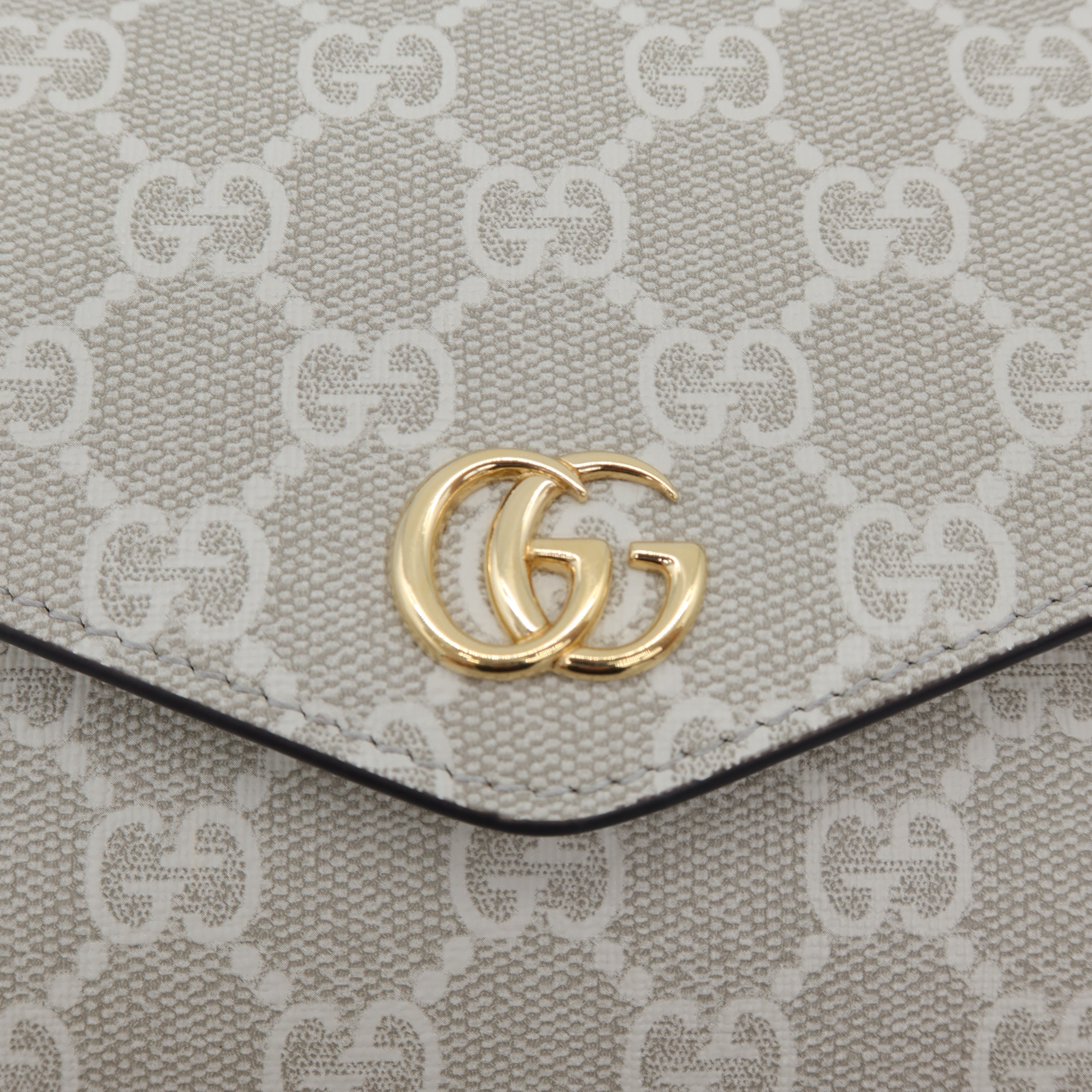 Close-up of a beige and off-white GG Supreme canvas pouch with a gold-tone interlocking G logo clasp on a clean white background.