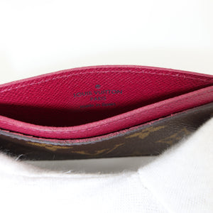 Close-up of the interior of a Louis Vuitton card holder or wallet, showing a deep magenta-pink leather lining with the embossed 'LOUIS VUITTON PARIS' logo and the brand's classic brown monogram canvas along the edge.