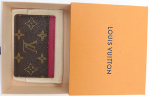 A Louis Vuitton monogram card holder wallet with a pink leather accent, presented inside its beige box next to an orange Louis Vuitton lid on a white background.