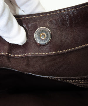 Close-up of a dark brown leather belt with a silver-toned snap button, held by a white-gloved hand.
