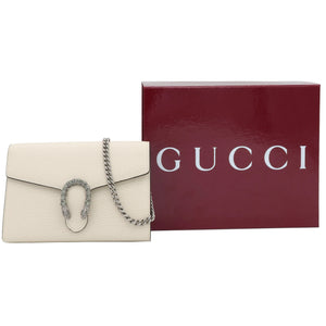A Gucci flap shoulder bag in off-white leather with a silver-tone chain strap and snake logo clasp, displayed next to its dark red Gucci box on a light gray background.