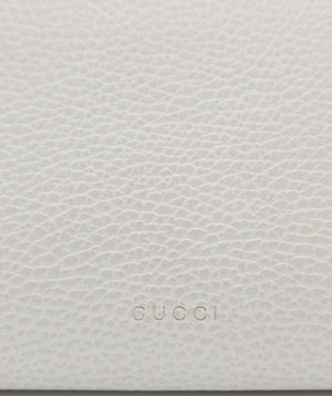 Close-up of a light beige pebbled leather surface with the embossed Gucci logo centered near the bottom.