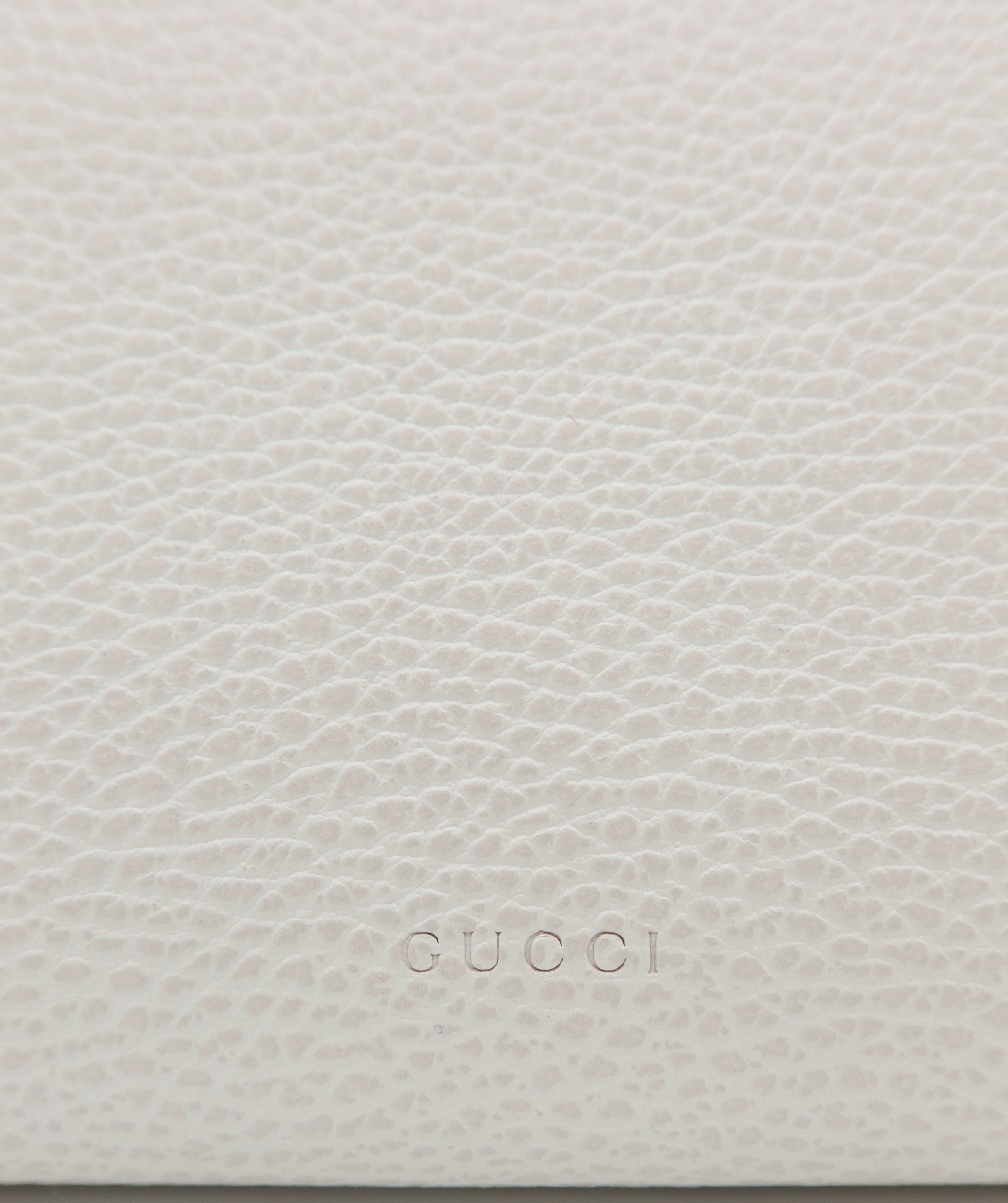 Close-up of a light beige pebbled leather surface with the embossed Gucci logo centered near the bottom.