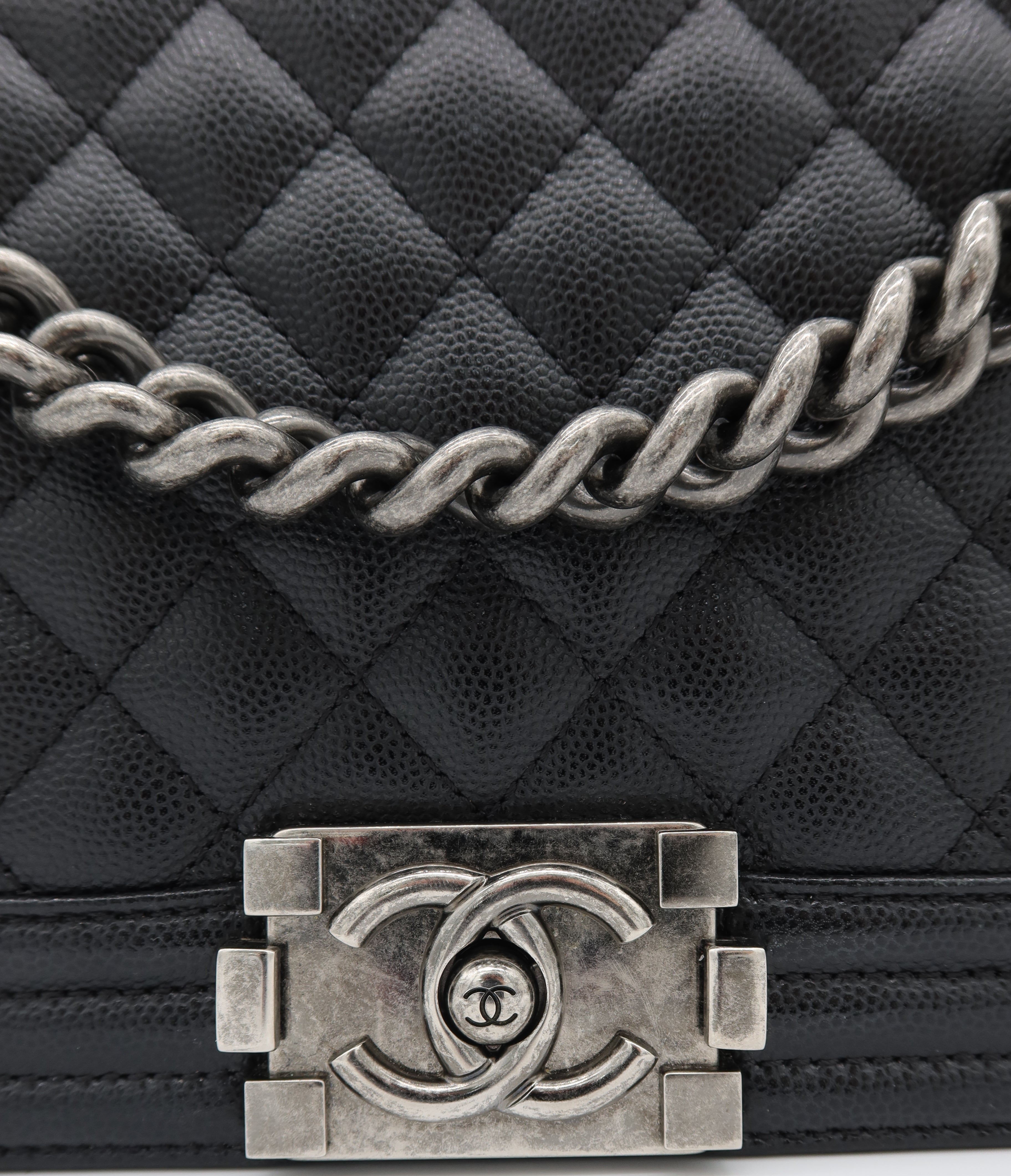 Close-up of a black quilted leather handbag with a silver-tone chain strap and a prominent interlocking CC turn-lock clasp, showing the Chanel logo.