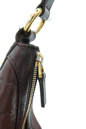 Close-up detail of a dark brown leather handbag showing a gold-tone metal ring, zipper pull, and gold zipper track against a plain white background.