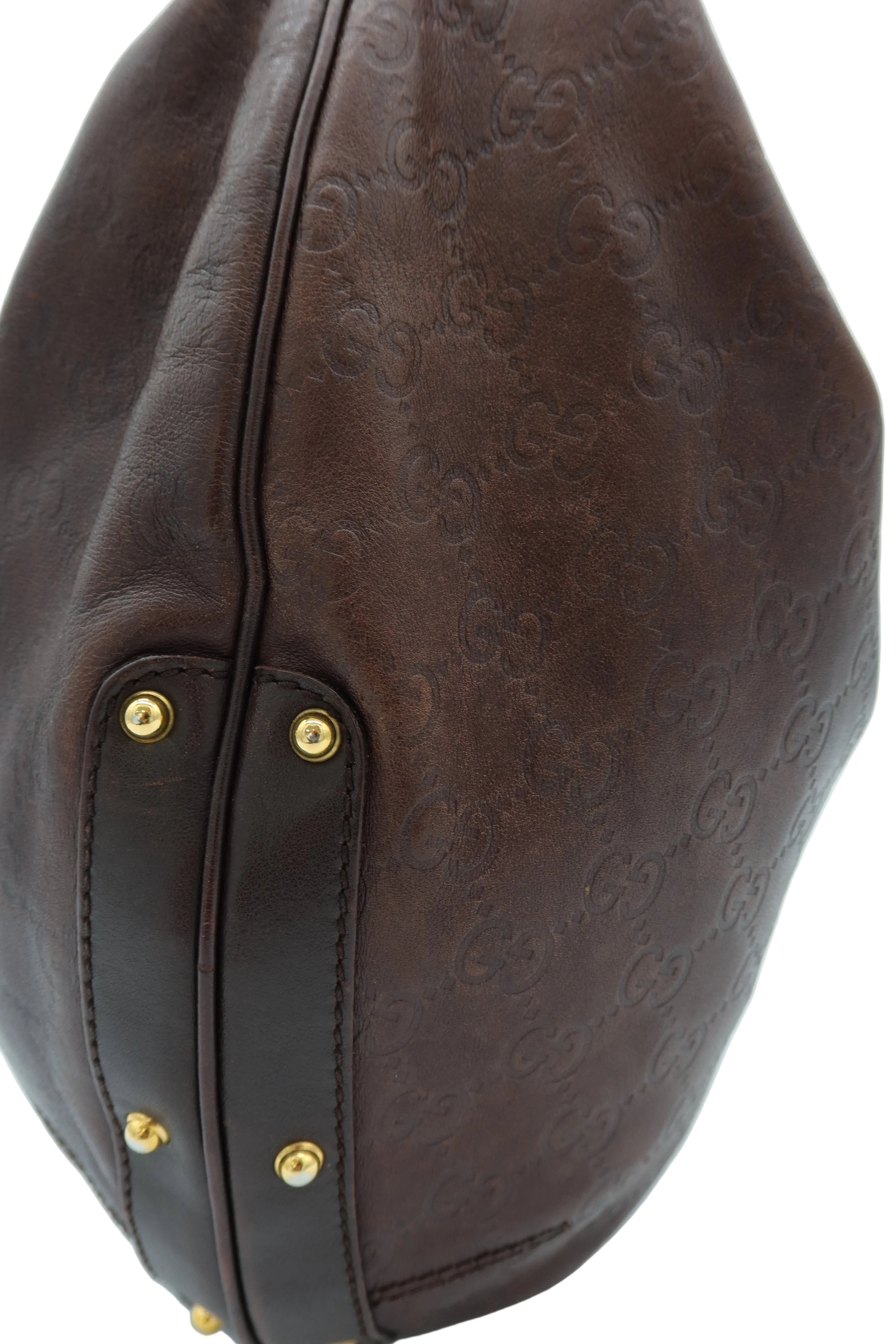 Close-up of a dark brown leather handbag featuring an embossed monogram pattern and gold-tone rivets on a white background.