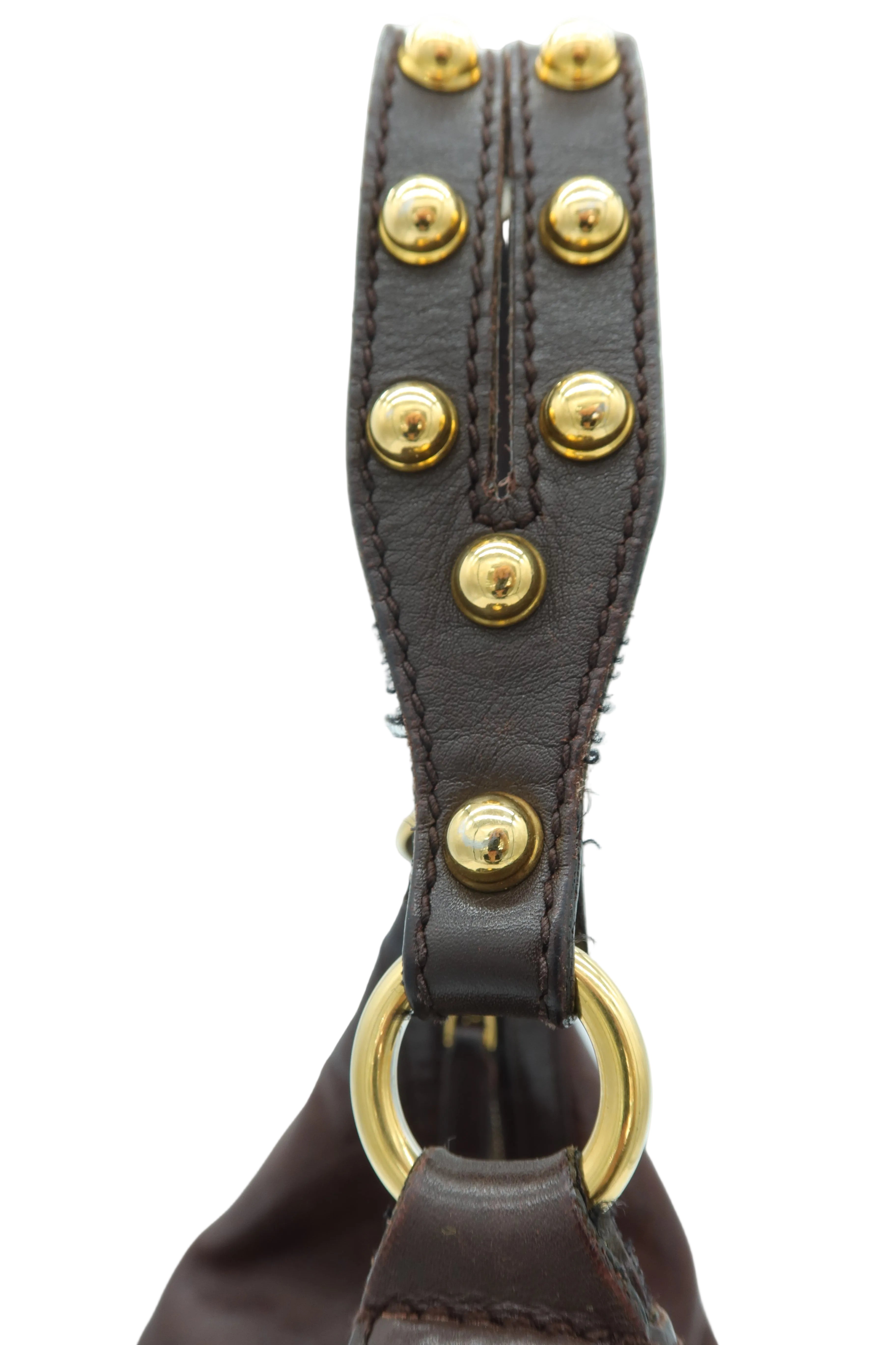 Close-up of a dark brown leather strap with gold-tone metal studs and a matching gold-tone ring hardware, set against a plain light background.