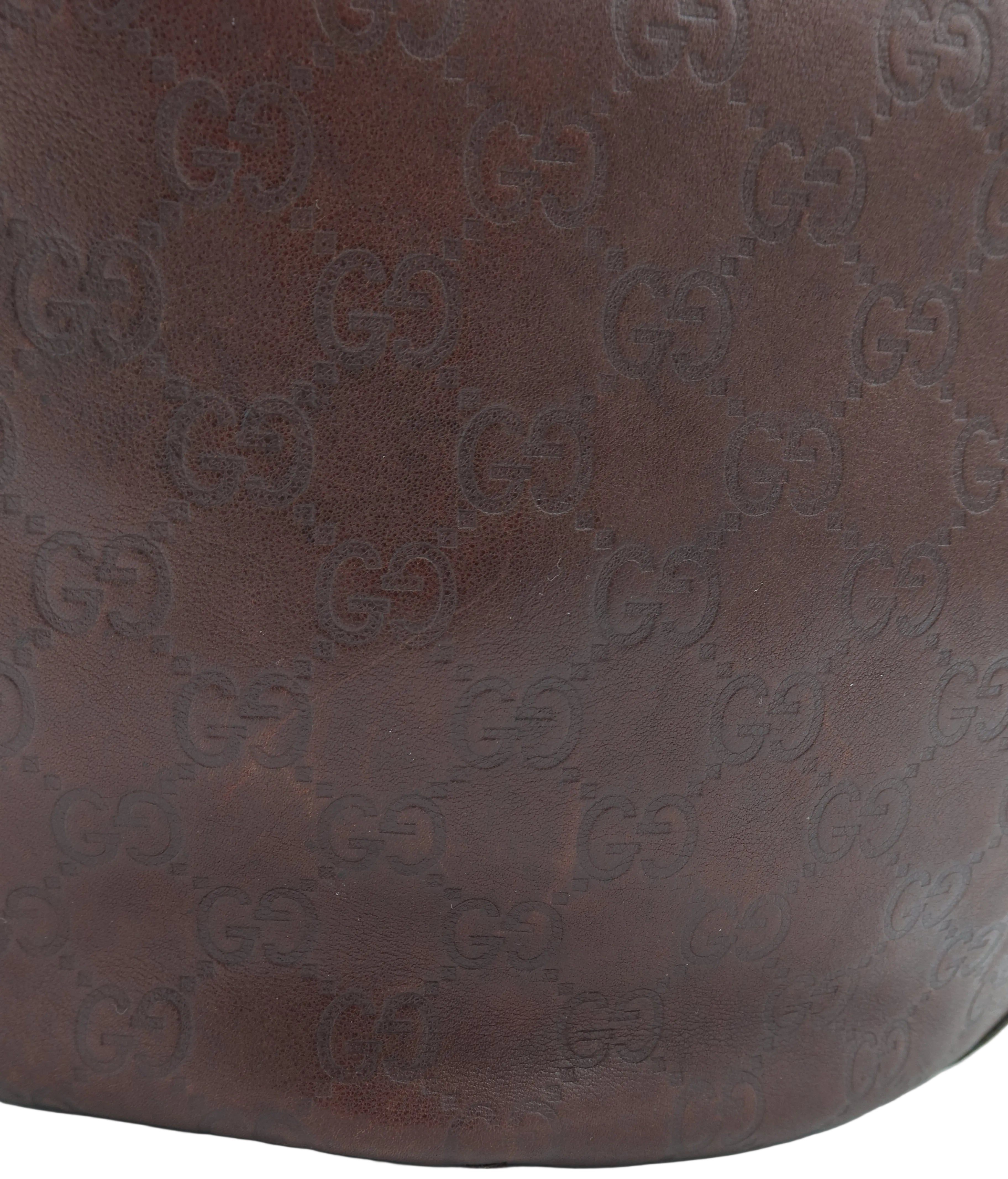 Close-up of a brown leather item featuring an embossed repeating interlocking G pattern, likely Gucci monogram, on a white background.