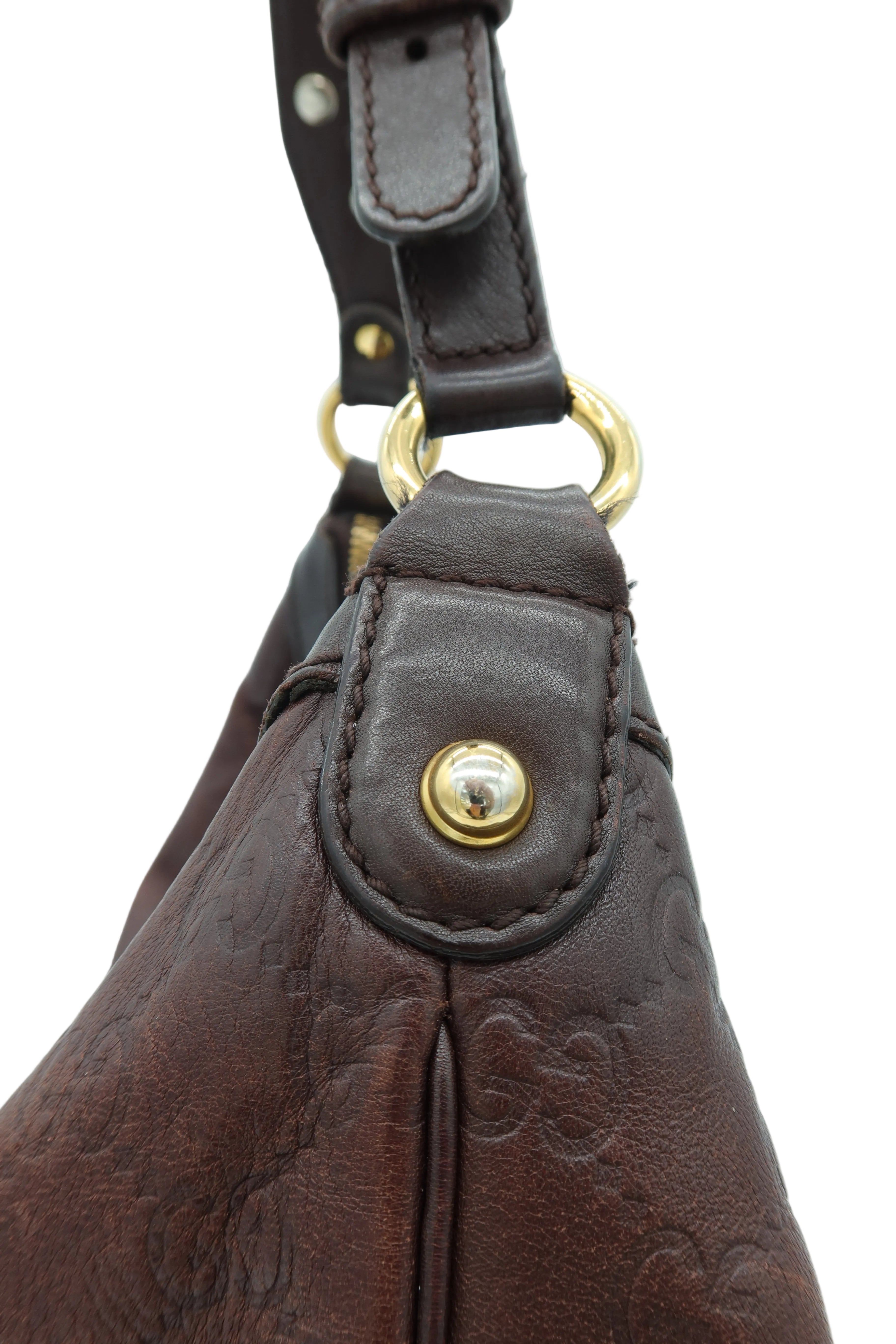 Close-up of a dark brown embossed leather handbag showing a gold-tone snap button closure and a matching leather strap with gold hardware against a light background.