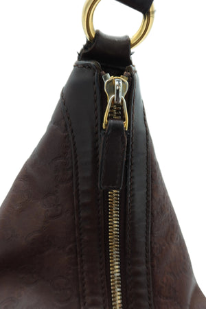 Close-up of a dark brown leather shoulder bag with an embossed monogram pattern, a gold-tone zipper pull, and a gold-tone metal ring at the top, set against a plain light background.