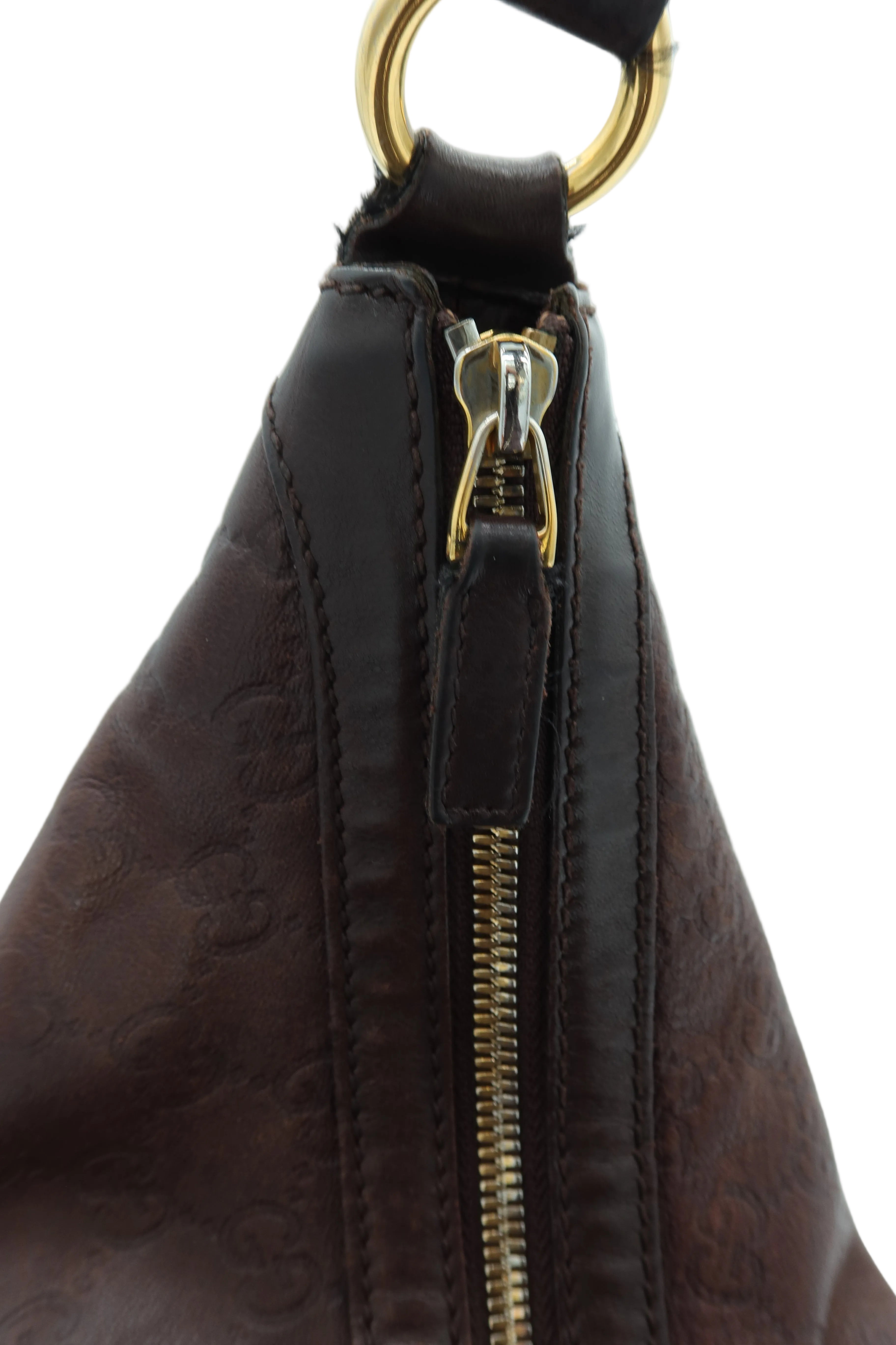 Close-up of a dark brown leather shoulder bag with an embossed monogram pattern, a gold-tone zipper pull, and a gold-tone metal ring at the top, set against a plain light background.