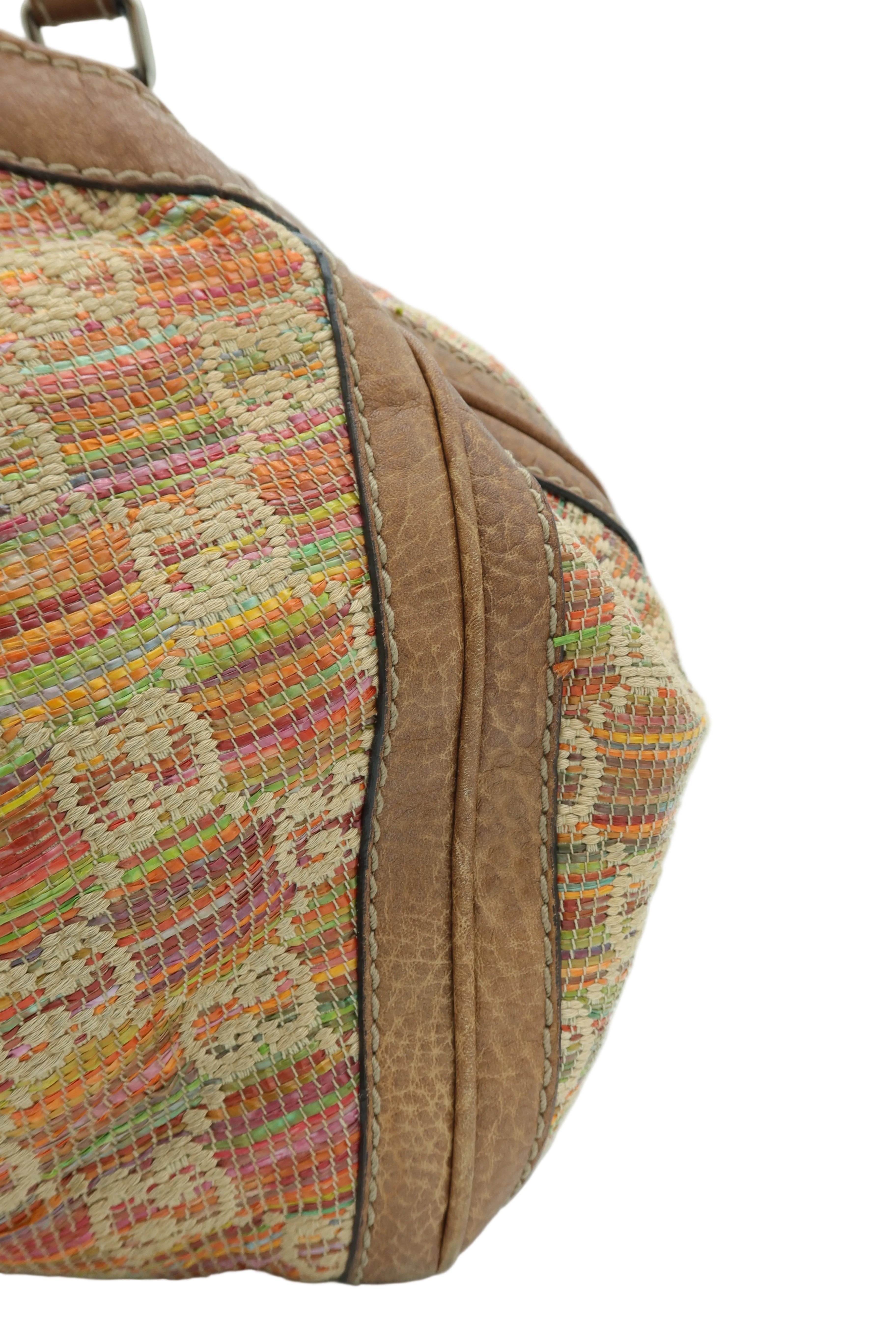 Close-up of a vintage woven handbag corner showing a multicolor striped patterned fabric and tan leather trim on a white background.