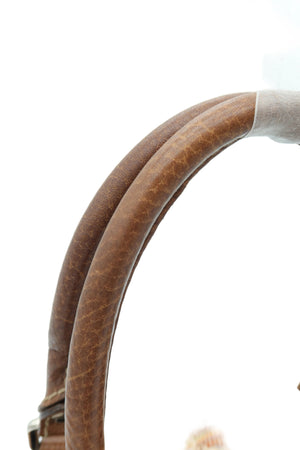Close-up detail of a brown leather shoulder strap with a textured finish and a small portion of a patterned bag body visible against a bright white background.