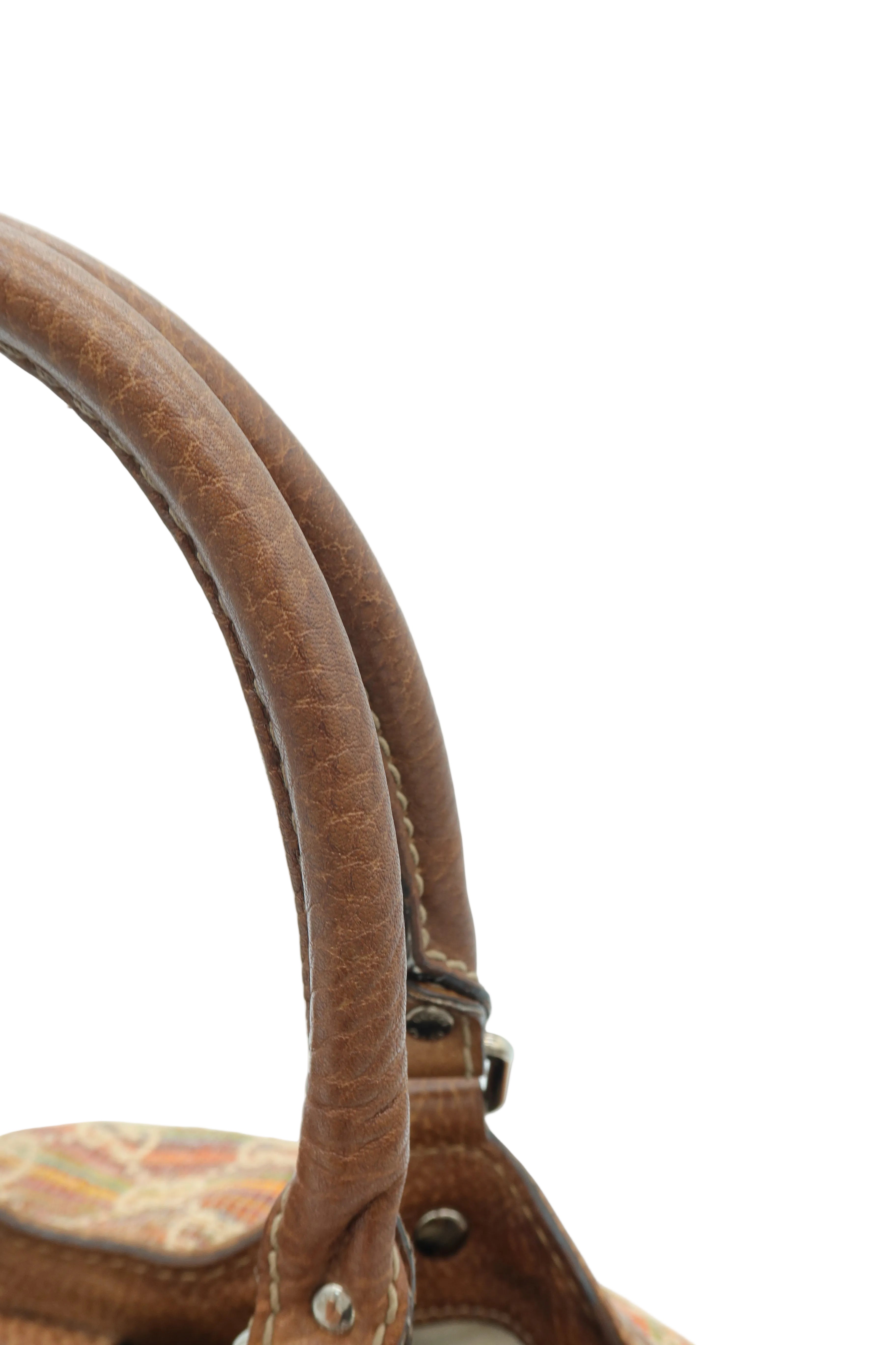 Close-up detail of a brown leather handbag handle with visible stitching and hardware, set against a plain light background.