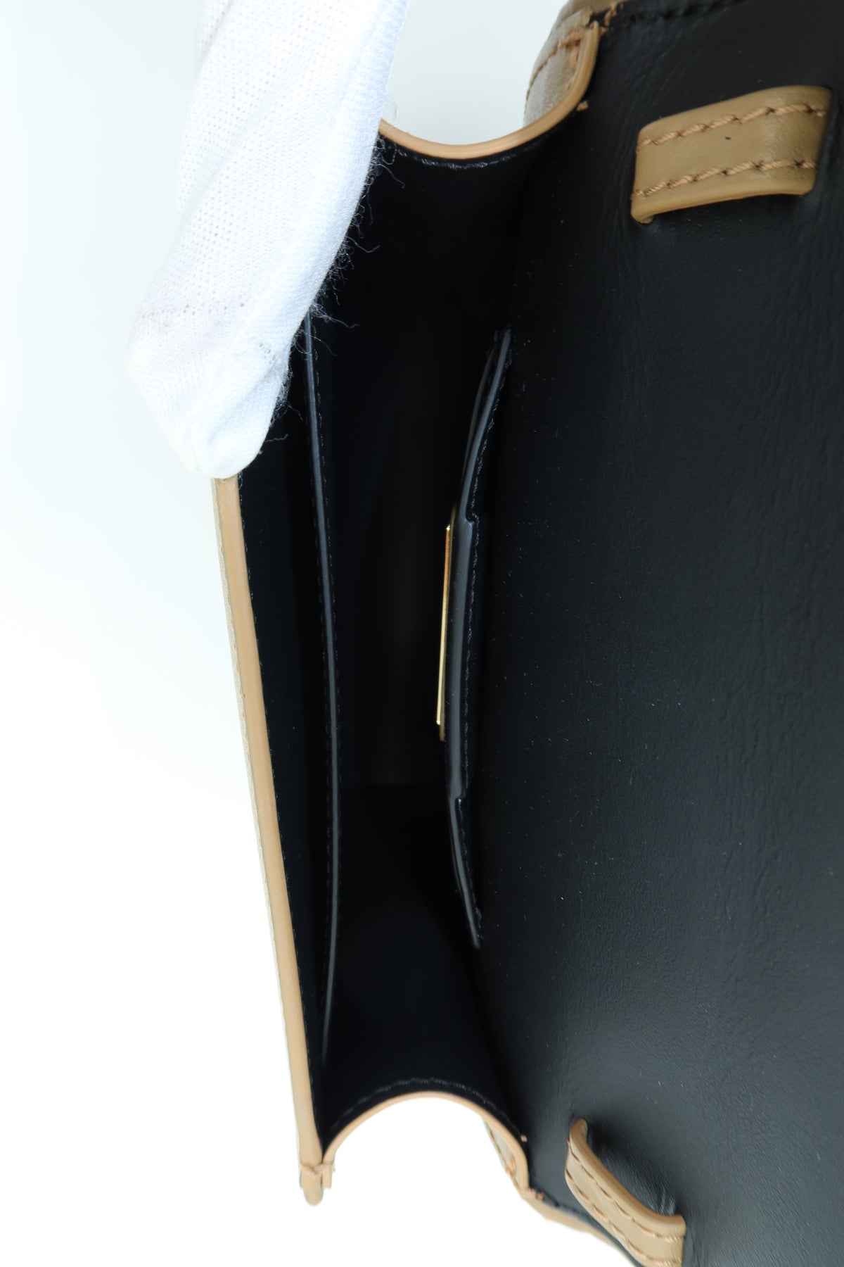 Close-up of the interior of a black leather handbag with tan trim and a small gold-tone metal accent, shown against a white background with a white glove partially visible.