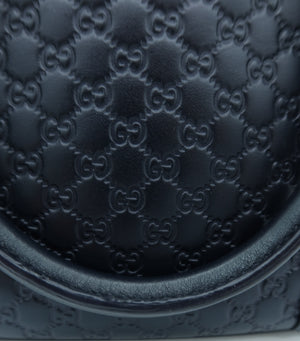 Close-up of a black leather handbag featuring the embossed Gucci GG monogram pattern and a curved top edge.