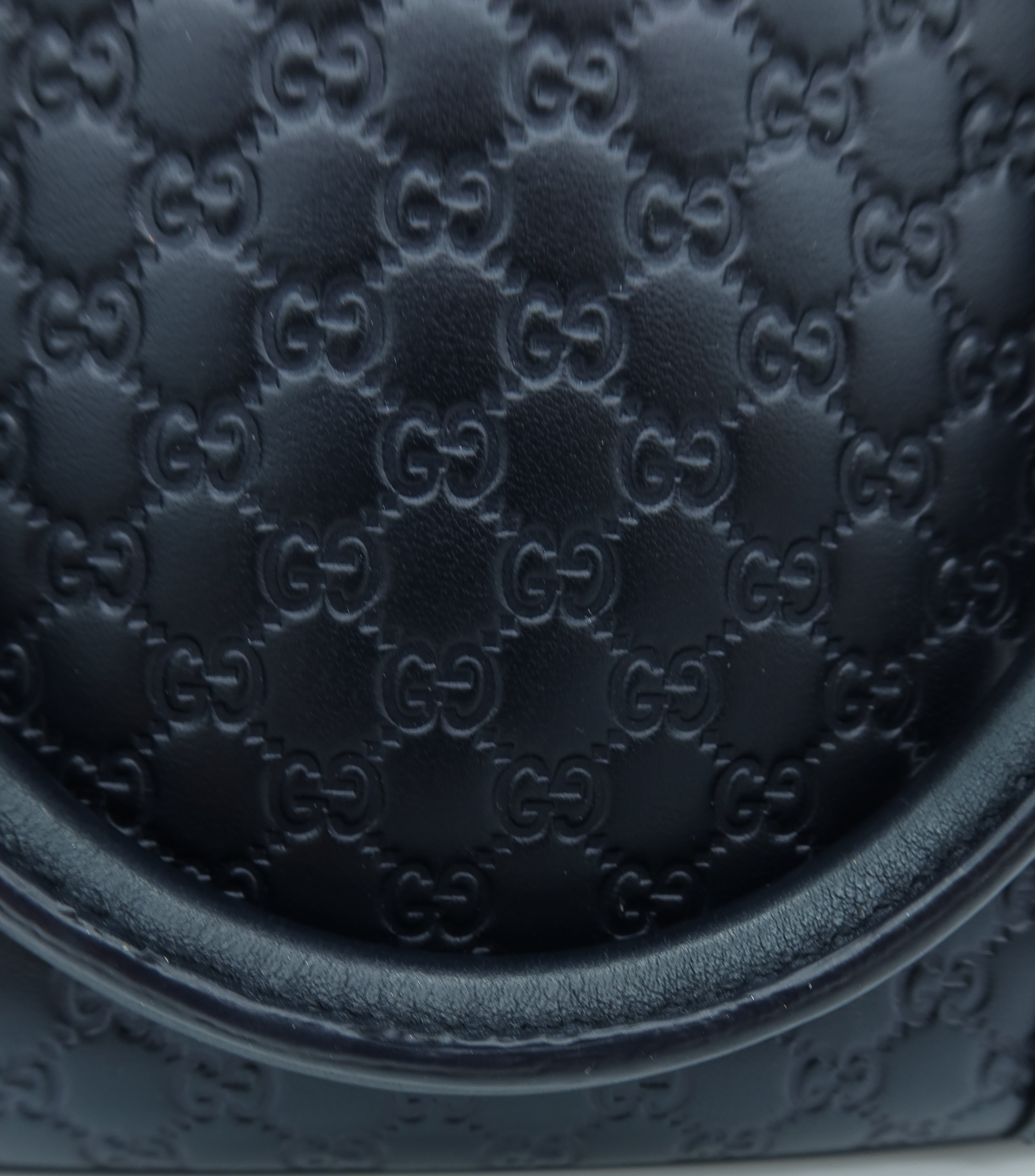 Close-up of a black leather handbag featuring the embossed Gucci GG monogram pattern and a curved top edge.