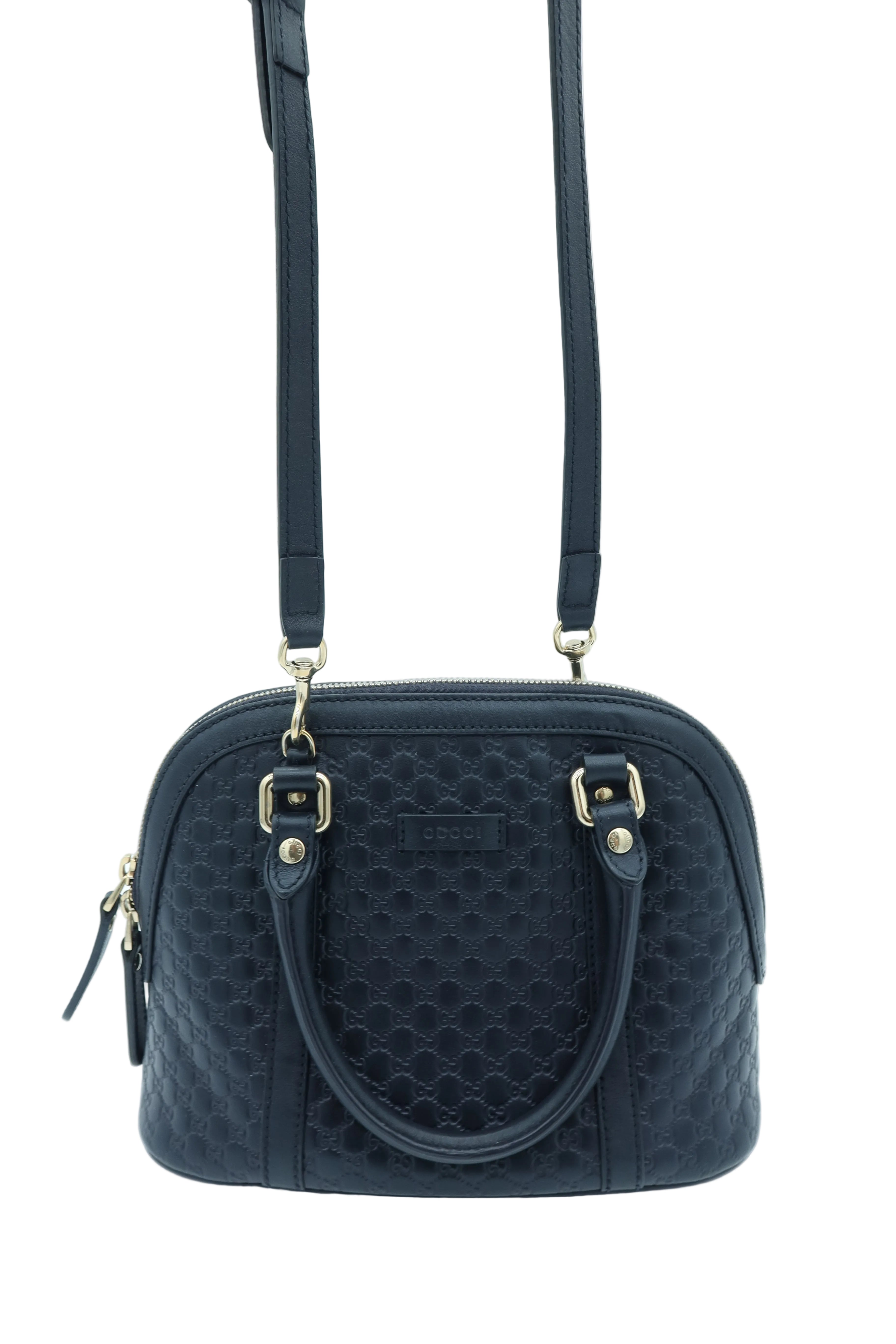 A black textured dome handbag with a top handle, a detachable shoulder strap, and gold-tone hardware, shown against a light blue studio background.