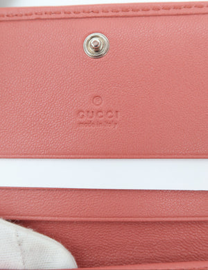 Close-up of a Gucci leather wallet or card holder in a dusty pink color, showing the pebbled texture, a silver-tone snap button, and the embossed Gucci logo.