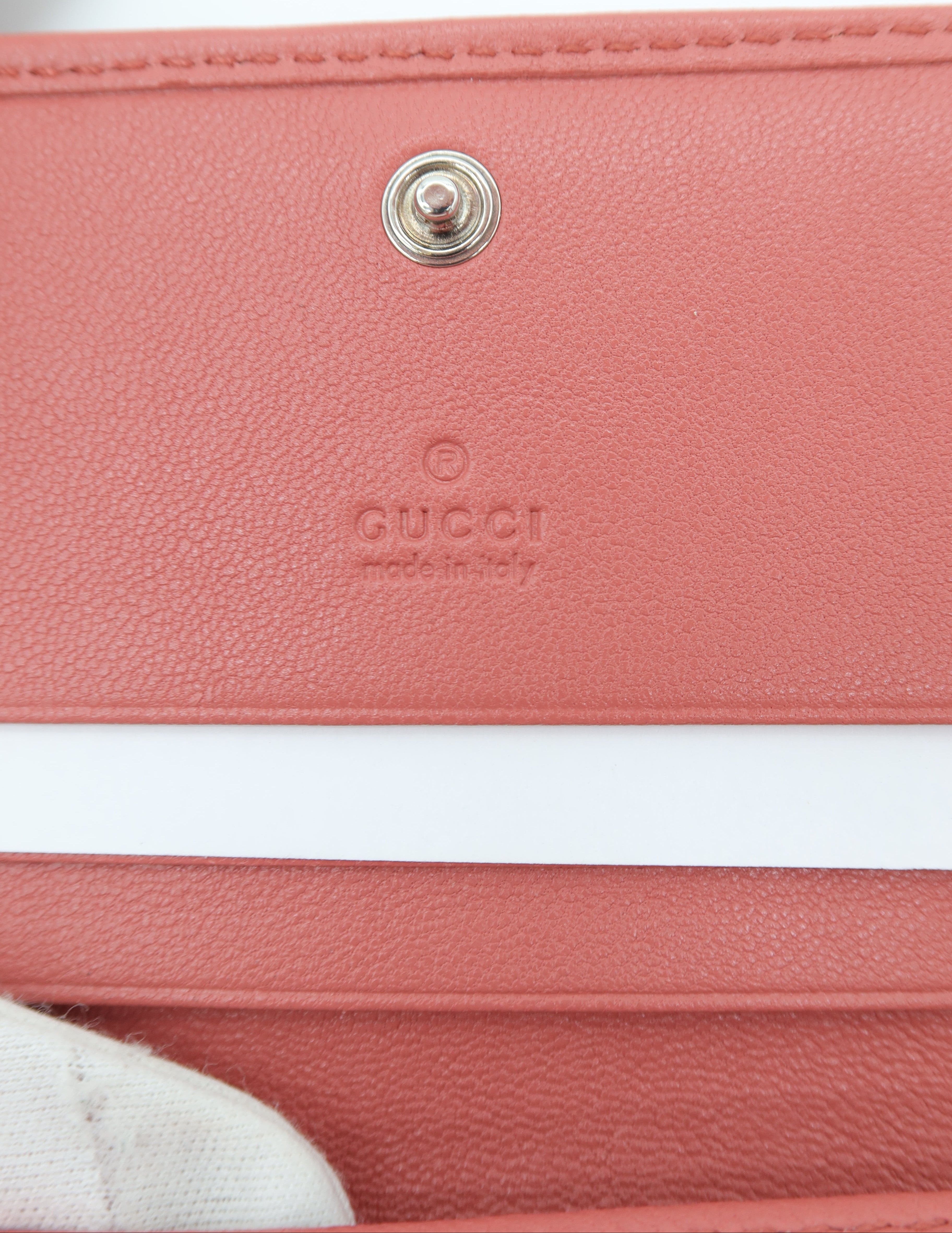 Close-up of a Gucci leather wallet or card holder in a dusty pink color, showing the pebbled texture, a silver-tone snap button, and the embossed Gucci logo.