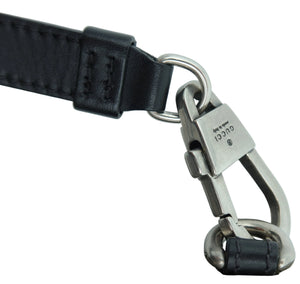 Close-up of a Gucci strap attachment with a silver-tone metal clasp engraved with the brand name, connected to a black leather strap on a light gray background.