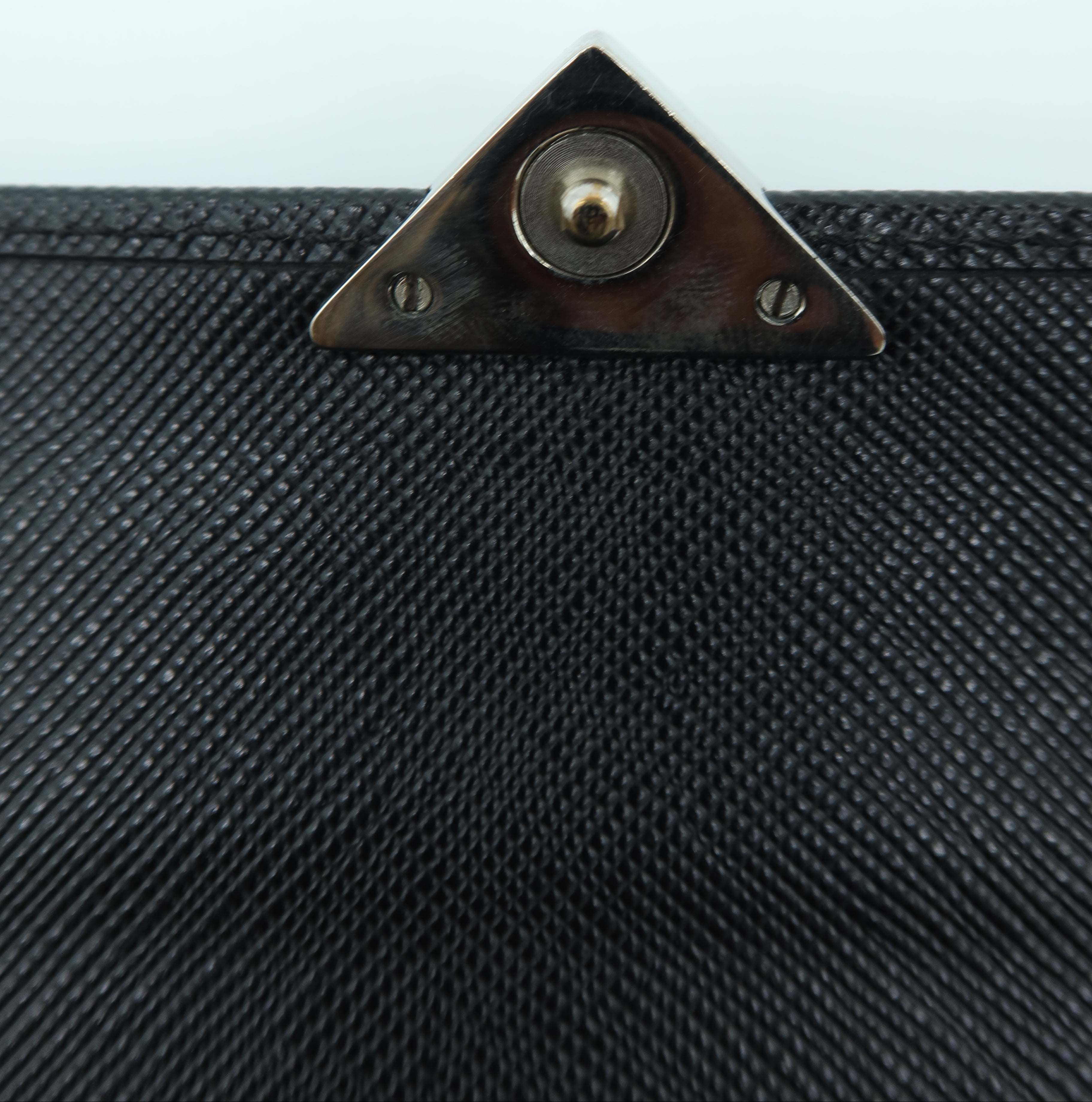 Close-up of a black textured fabric item with a triangular metal snap closure at the top center, set against a plain light background.