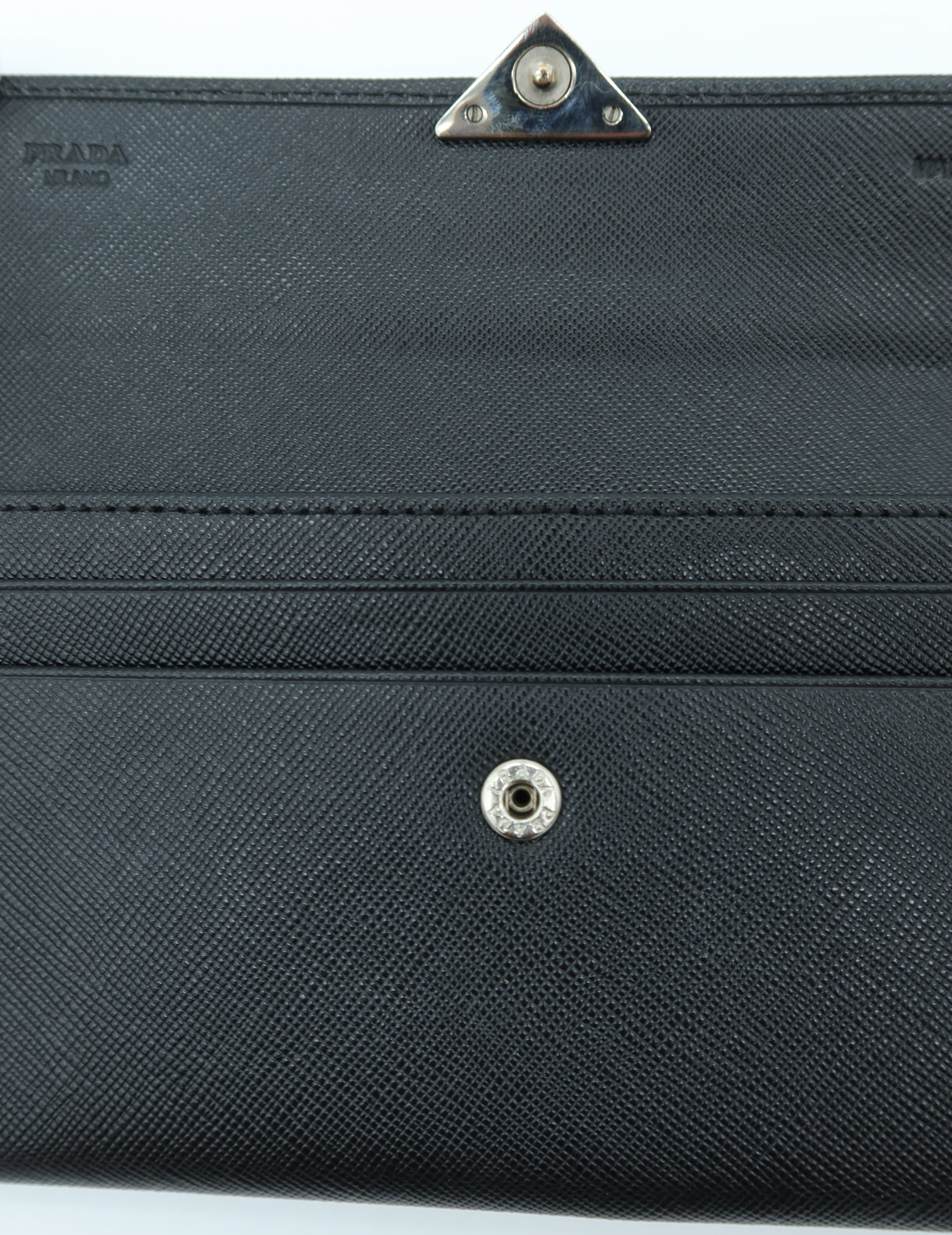 Close-up of a black textured leather or faux-leather accessory with a snap button closure and a triangular metal clasp on a white background.