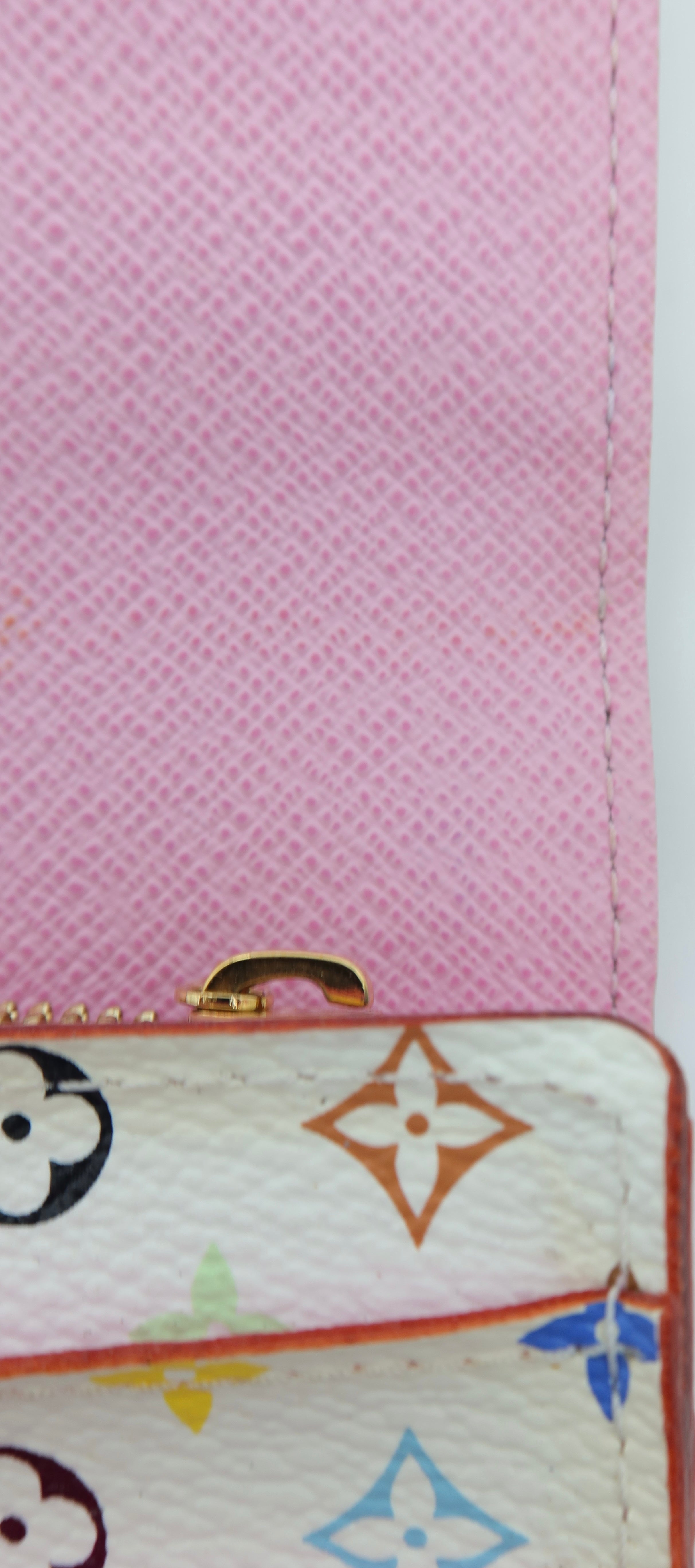Close-up of a Louis Vuitton wallet or pouch showing a pink textured interior flap and a cream exterior with multicolor monogram motifs and a gold-tone zipper pull.