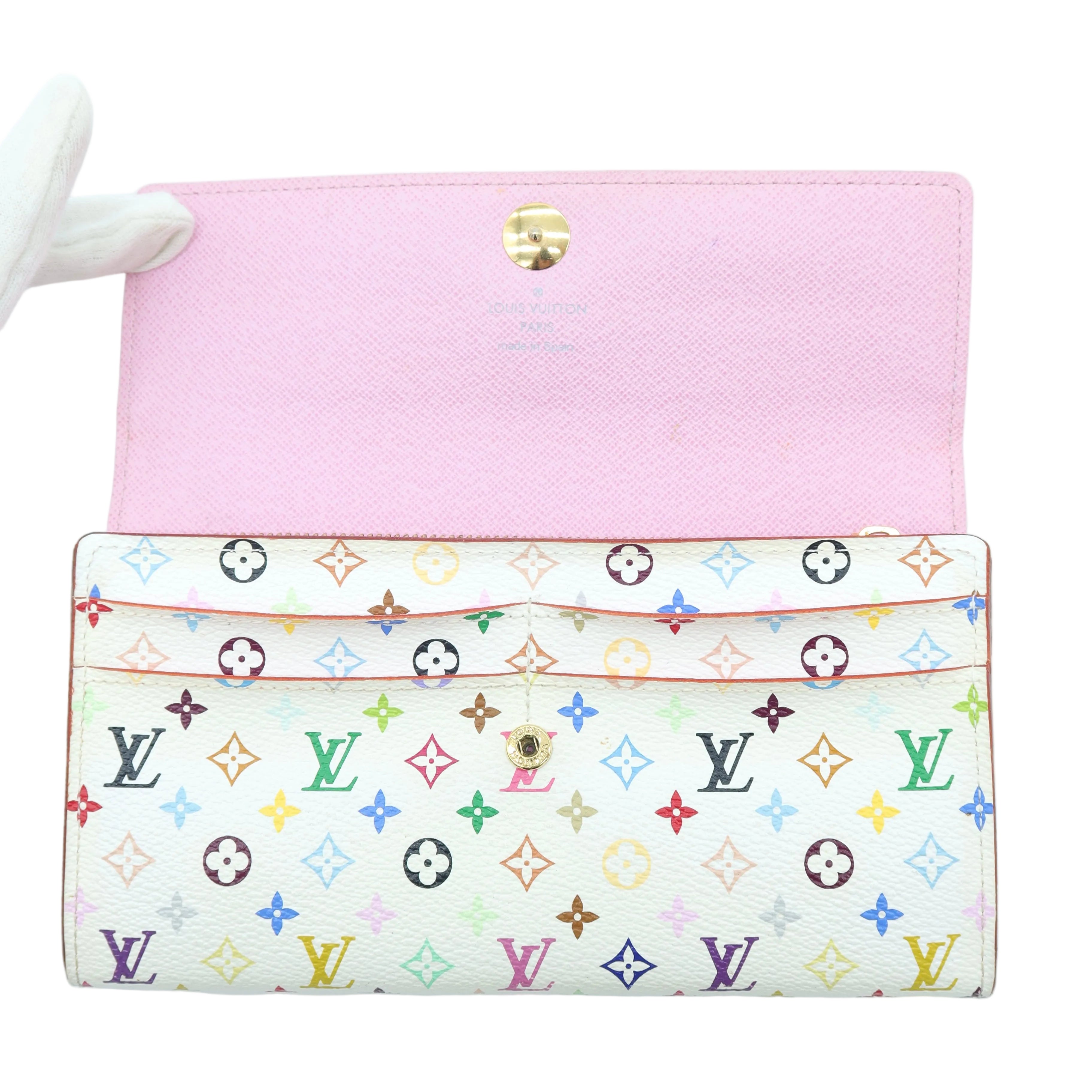 A Louis Vuitton monogram wallet or clutch shown open on a white background, with a pink interior flap and a cream exterior covered in multicolored LV monogram motifs.
