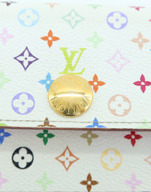 Close-up of a Louis Vuitton monogram canvas item, likely a wallet or pouch, featuring the classic multicolor monogram pattern on a white background with a prominent gold-tone circular metal emblem.