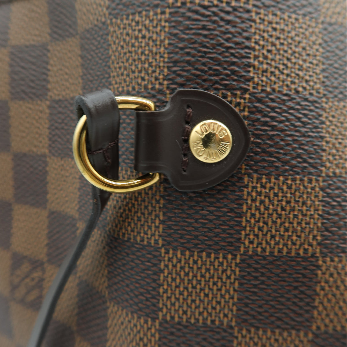 Close-up of a Louis Vuitton handbag in Damier Ebene canvas, showing the brown and tan checkered pattern, black leather trim, and gold-tone hardware.