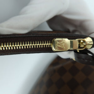 Close-up of a Louis Vuitton Damier canvas bag with a brown and black checkered pattern, featuring a gold-tone metal zipper with a gold LV logo pull, held by a white gloved hand.
