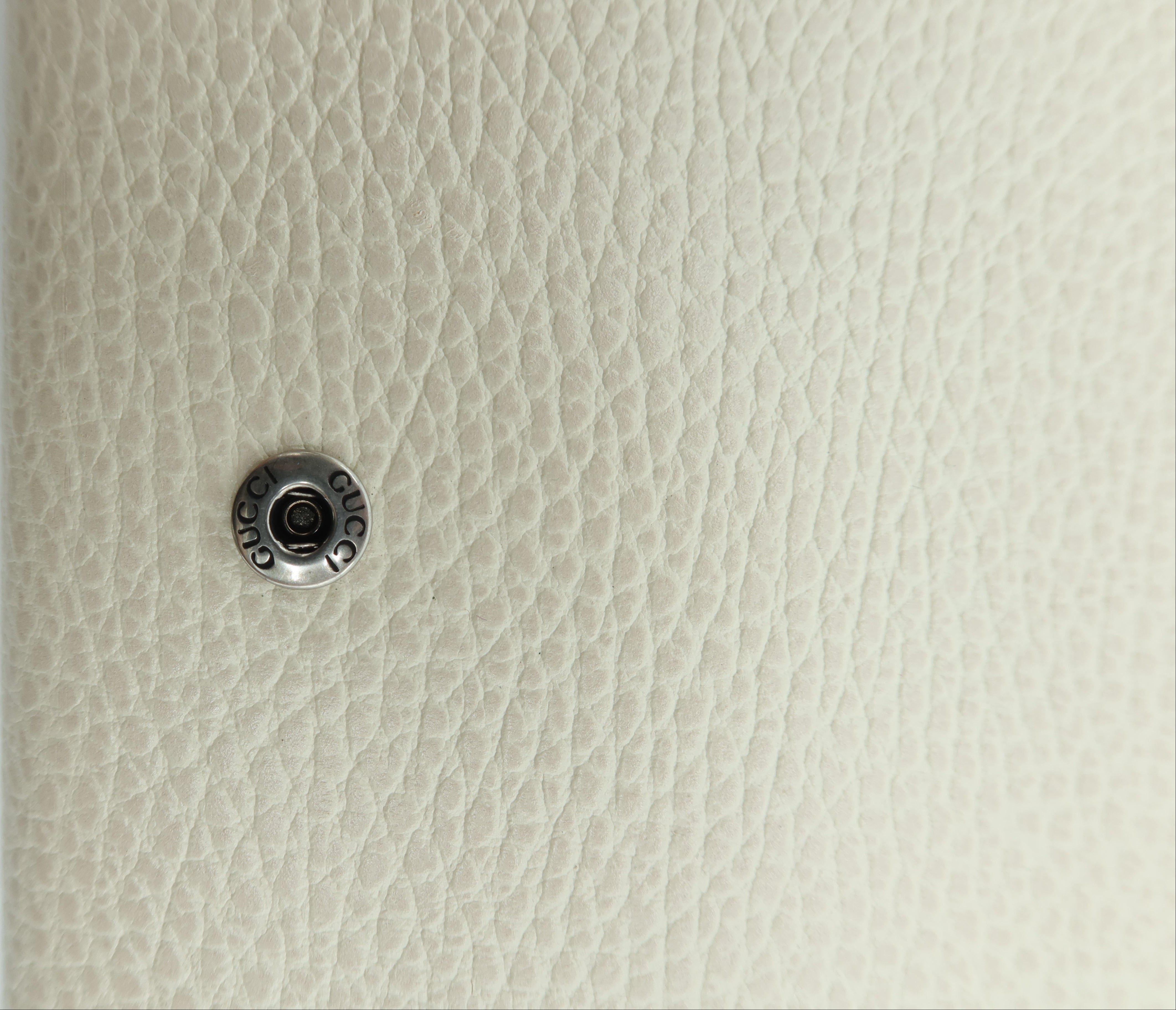 Close-up of a small round silver metal button or snap fastener attached to a textured off-white pebbled surface next to a plain white vertical edge.