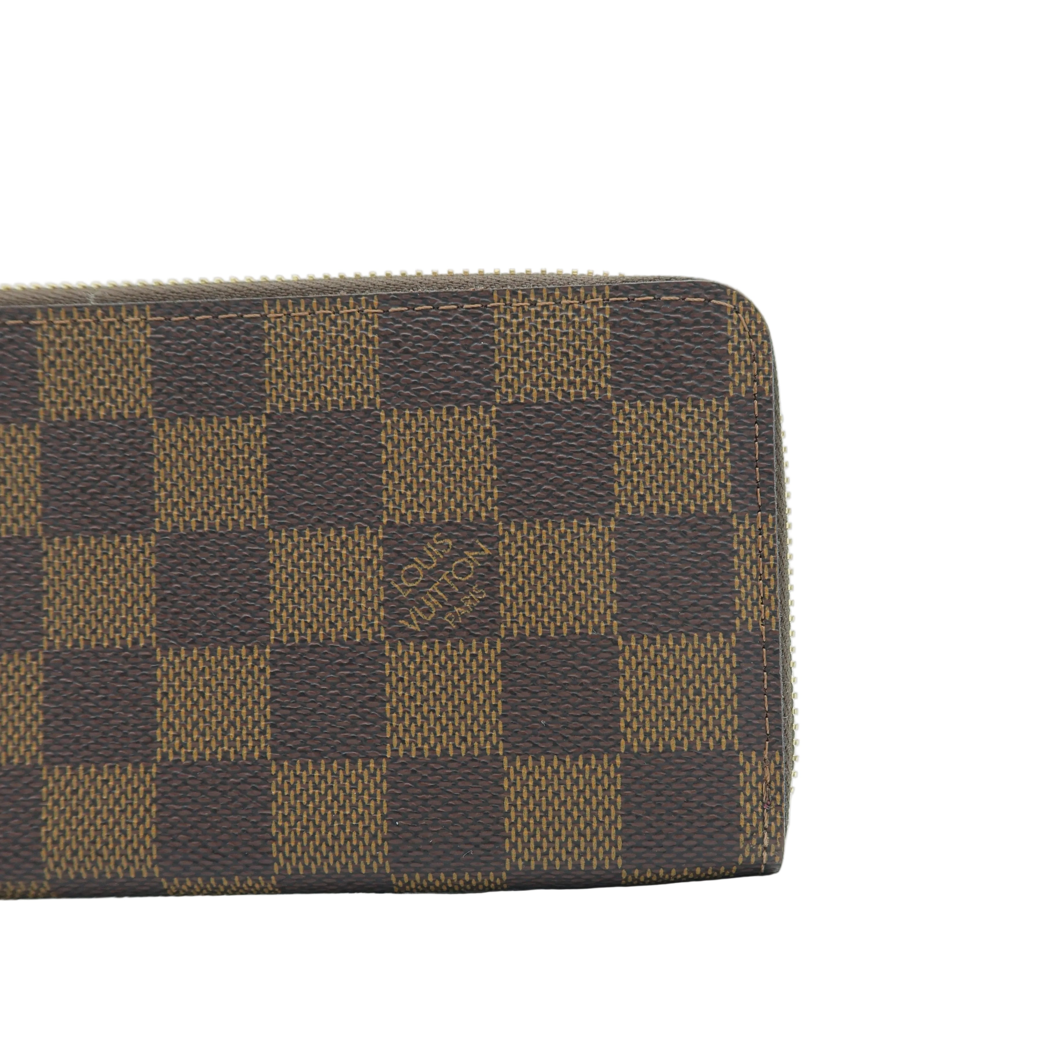 A close-up of a brown and tan checkered wallet, showing the classic Damier Ebene pattern and a small embossed logo on a white background.