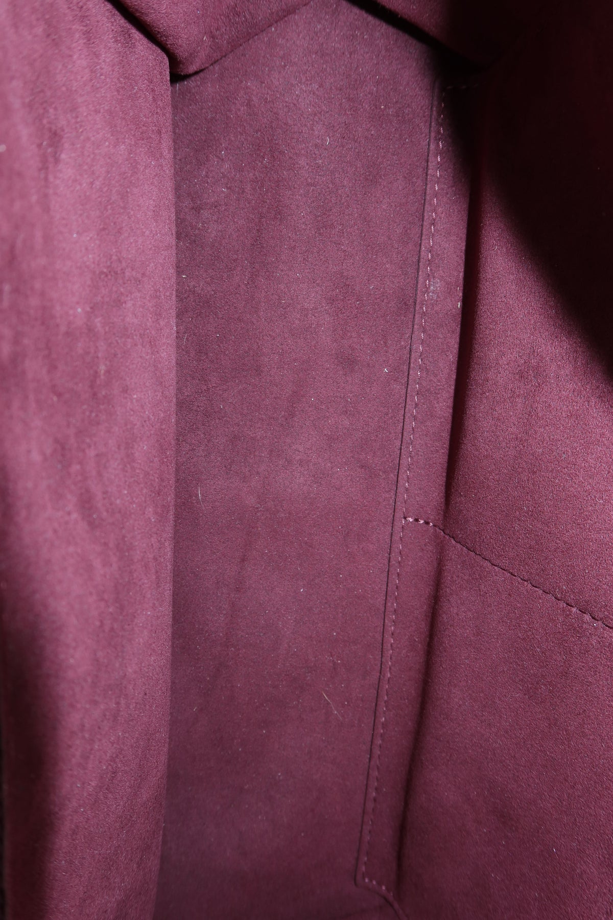 Close-up of a burgundy suede or microfiber fabric surface with stitched panel seams and a soft textured finish.