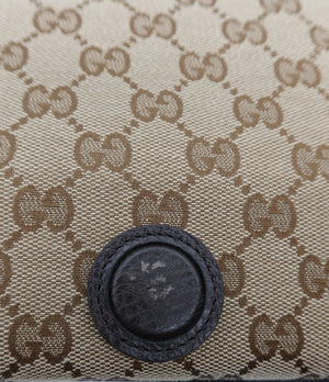 Close-up of a beige and brown GG Supreme canvas item with a dark brown leather button closure, showing the classic interlocking G pattern.