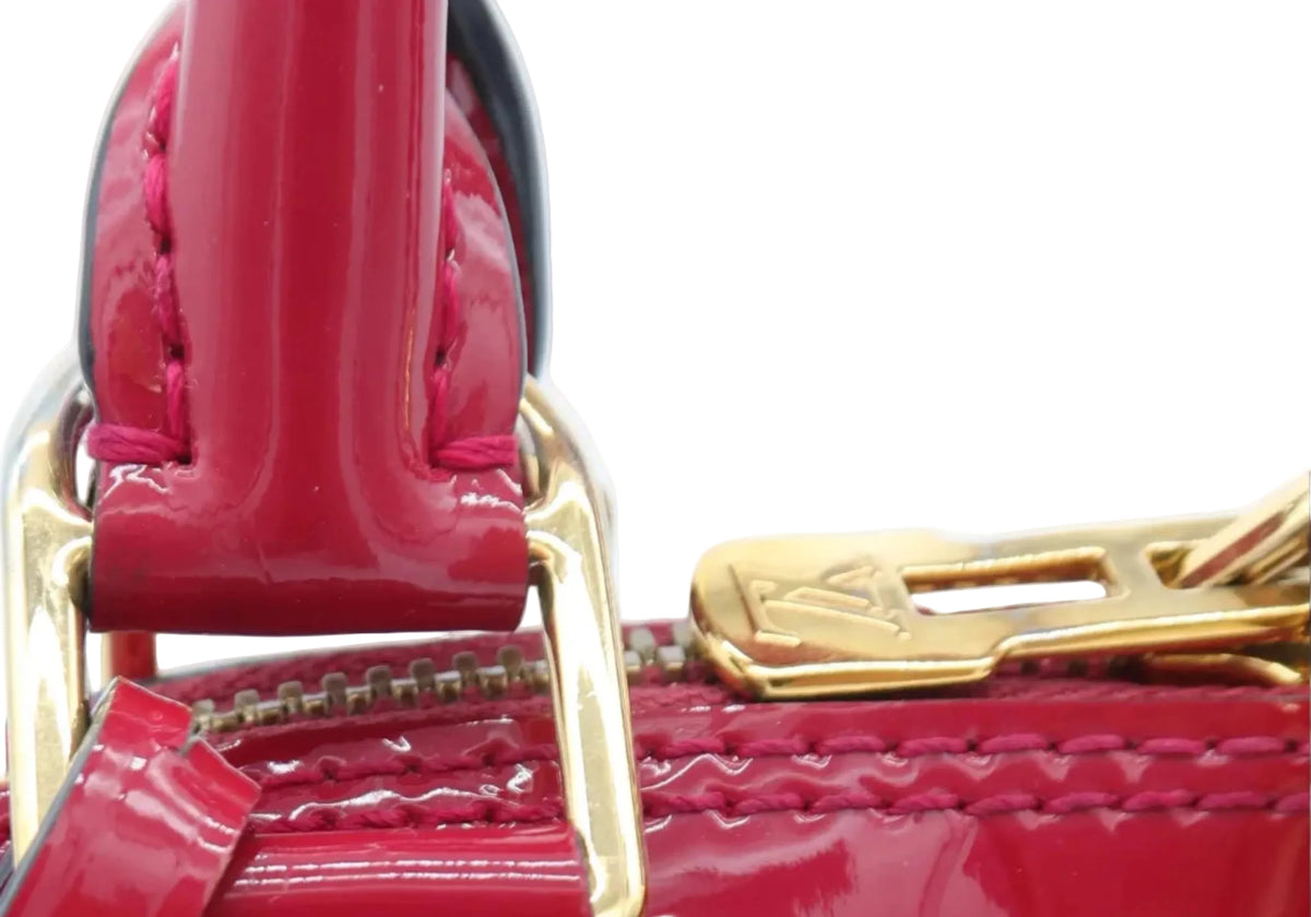 Close-up of a red Louis Vuitton handbag featuring the brand's signature monogram pattern, gold-tone hardware, and a leather strap detail against a white background.