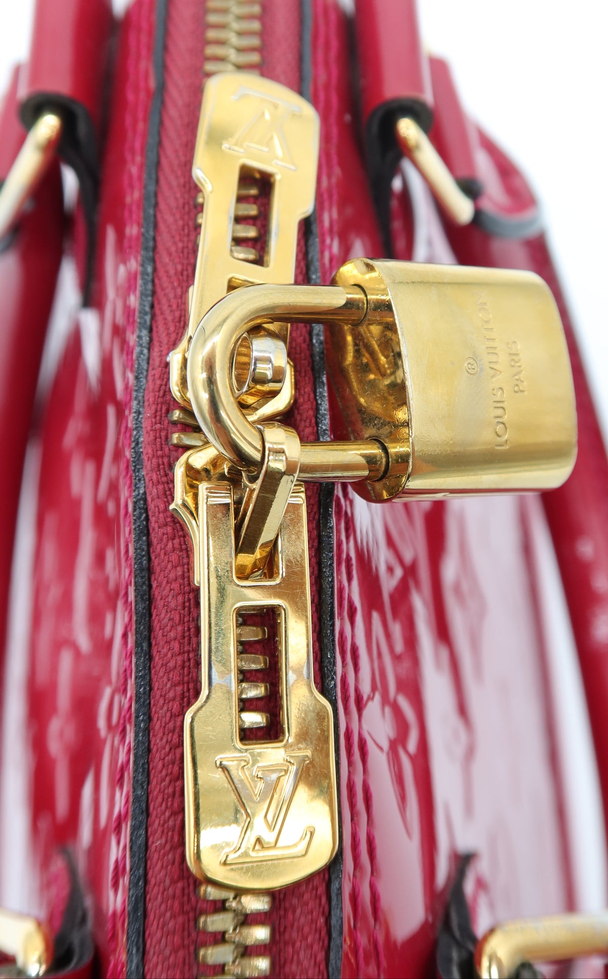 A close-up of a Louis Vuitton red patent leather bag featuring a gold-tone zipper, padlock, and hardware on a white background.