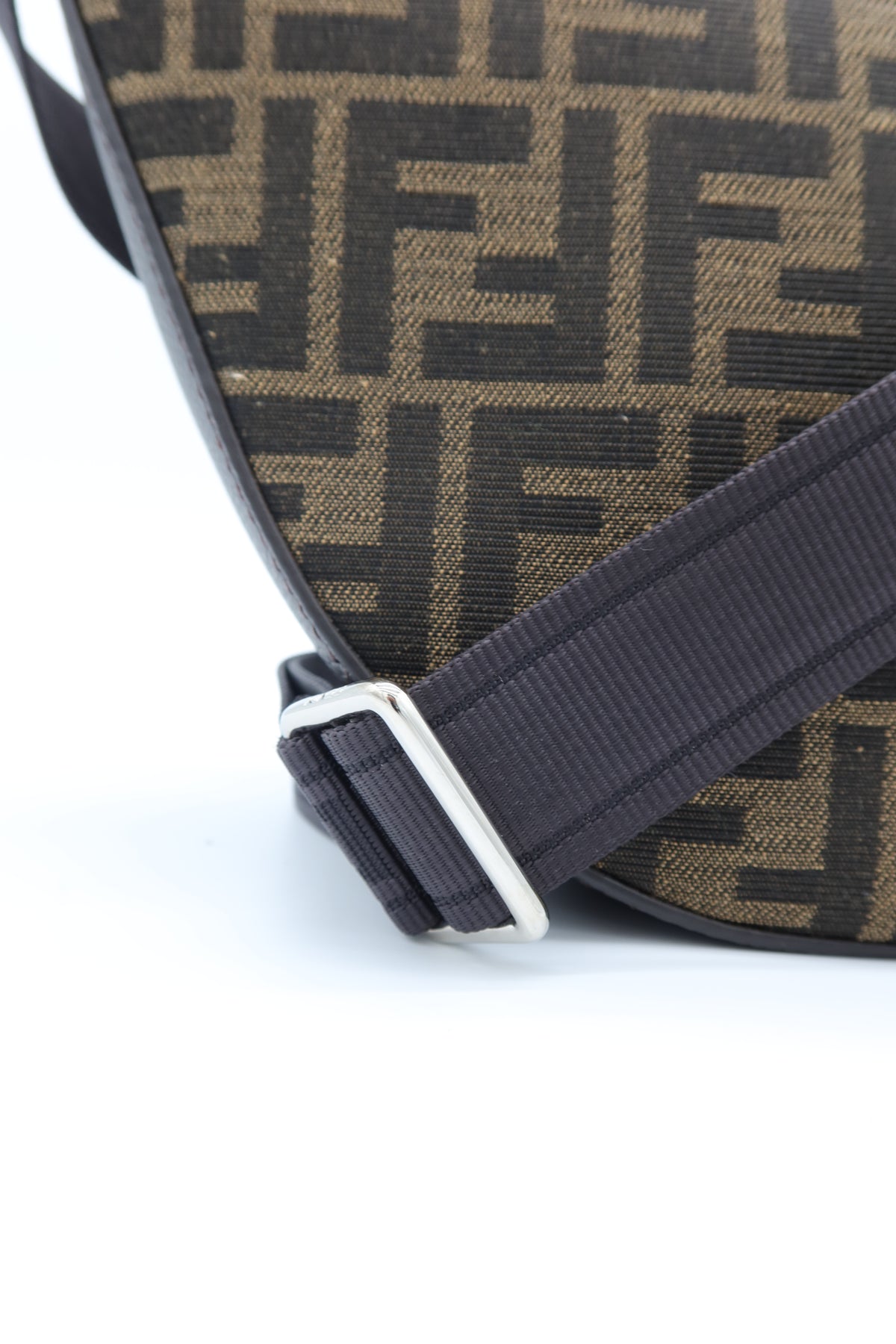 Close-up of a Fendi shoulder bag featuring the signature brown and black FF monogram canvas and a dark strap with a silver buckle, set against a plain white background.