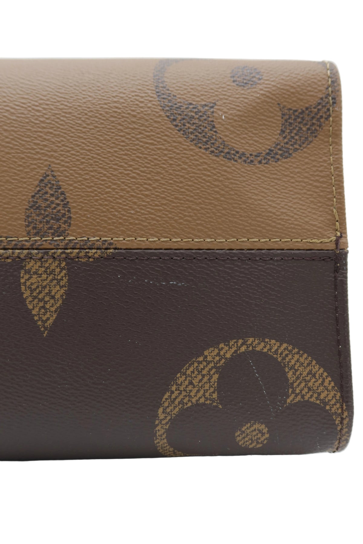 Close-up of a brown and tan monogram wallet or clutch with a pebbled leather texture and stitched edge, showing part of the Louis Vuitton-style floral monogram pattern.