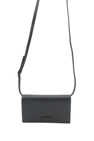 A black leather crossbody bag with a textured diamond pattern, featuring a thin black strap and a small rectangular metal plaque on the front, set against a plain white background.