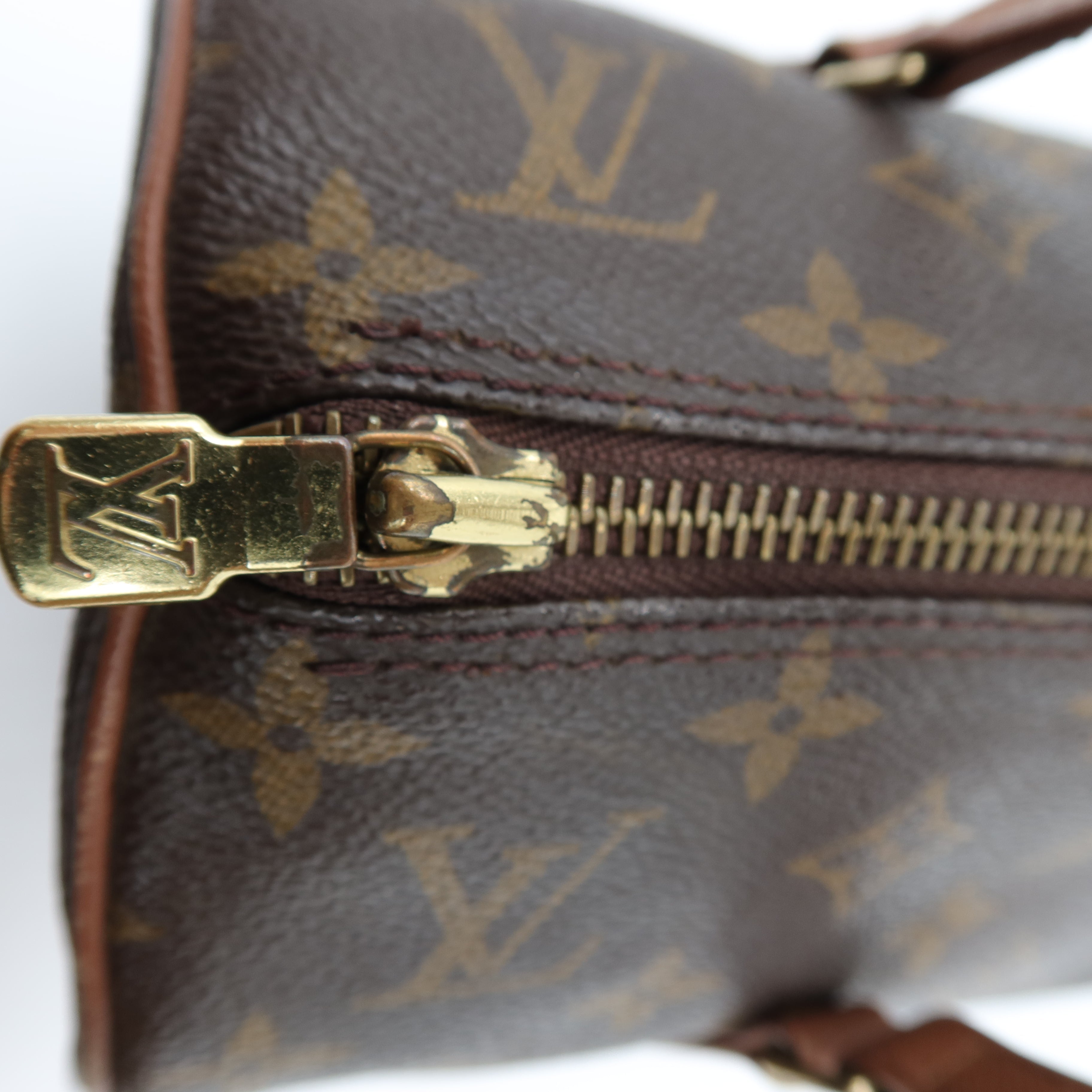 Close-up of a Louis Vuitton monogram canvas bag with a gold-tone metal zipper pull and zipper track on a white background.