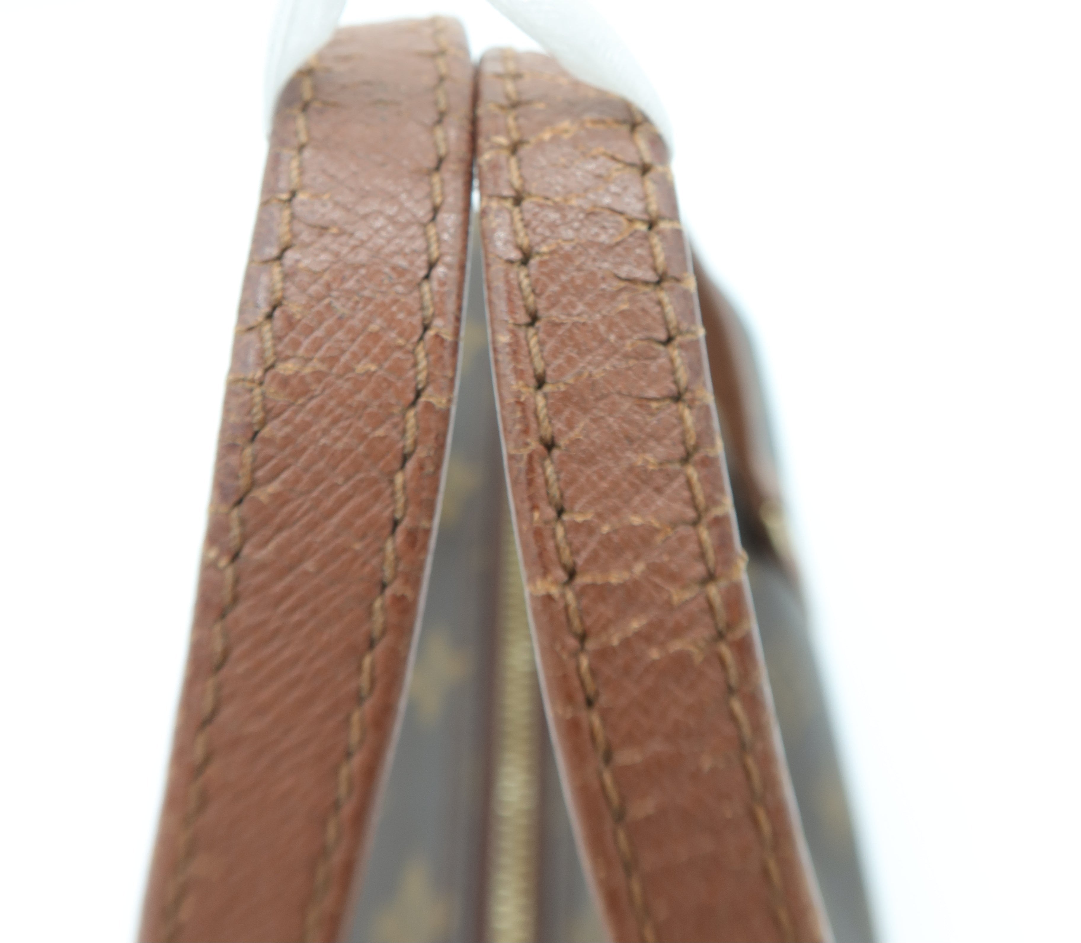 Close-up detail of a brown leather strap with fine stitching and a gold-toned zipper, attached to a light-colored bag against a white background.