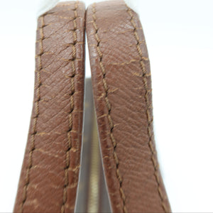Close-up of a brown leather strap with visible stitching and a white ribbon tied at the top, photographed against a bright white background.
