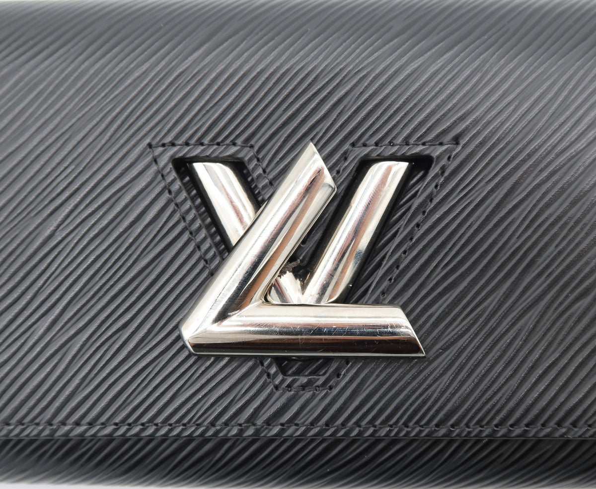 A close-up of a black textured leather Louis Vuitton wallet or clutch featuring the iconic silver-tone LV logo on the front.
