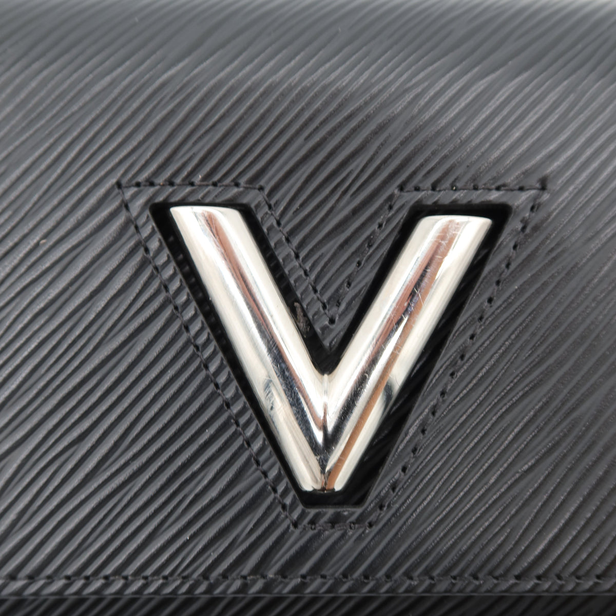 Close-up of a black textured leather wallet or clutch featuring a prominent polished silver-tone 'V' logo on the front.