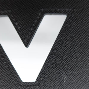 Close-up of a black textured leather item featuring a large, polished silver metallic 'V' logo, with a white circular element visible at the top edge.