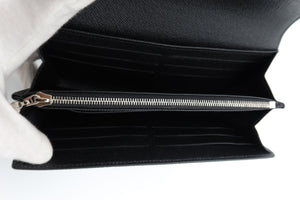 Black textured leather long wallet shown open, revealing multiple card slots and a silver zipper, held by a white-gloved hand against a white background.