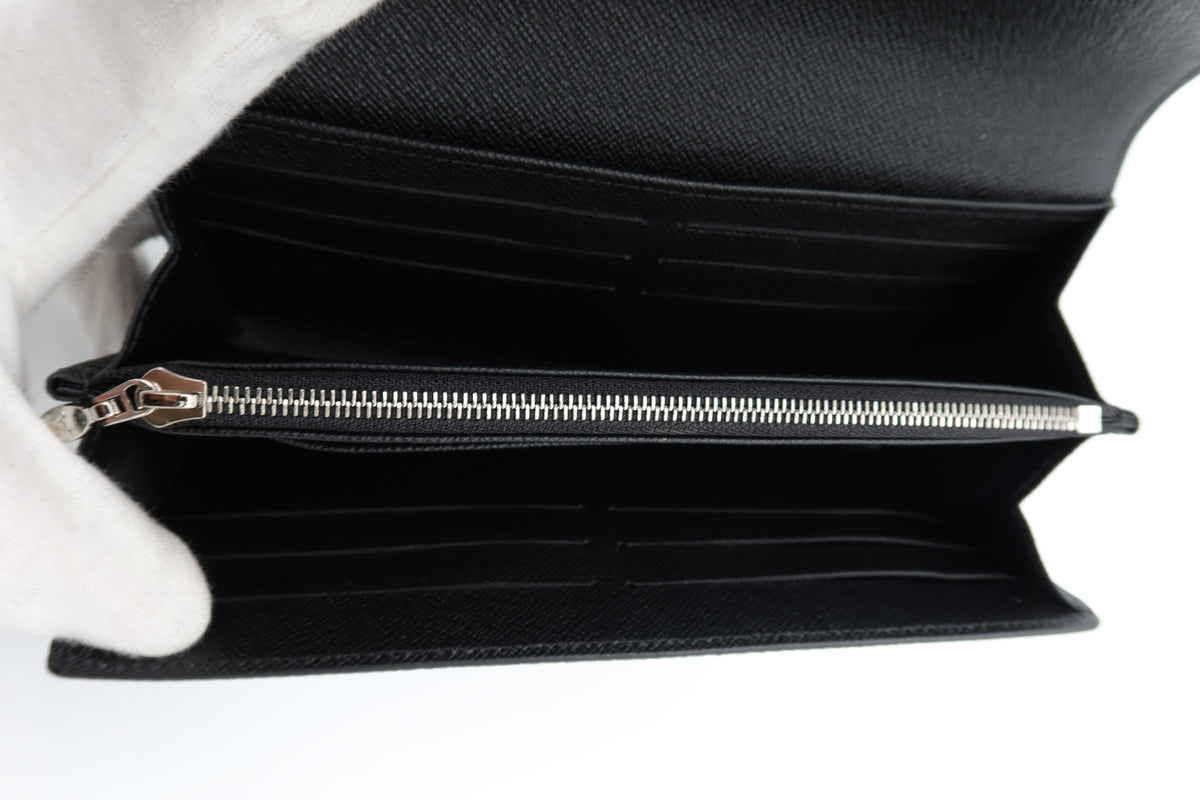 Black textured leather long wallet shown open, revealing multiple card slots and a silver zipper, held by a white-gloved hand against a white background.